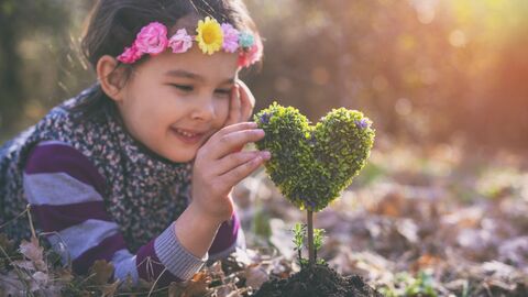 Kind liegt lachend auf dem Waldboden vor einem kleinen herzförmigen Baum