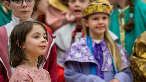 Ein verkleidetes Mädchen mit Sternsinger Kostüm und Krone, ein anderes kleines Mädchen daneben und weitere Kinder drumherim