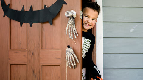 Ein Junge im Halloweenkostüm kommt lachend durch eine geuselig dekorierete Tür