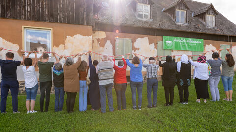 Die Mitglieder des Kulturcafé Gambach e. V. stehen vor ihrem Café, verbunden durch einen roten Faden, den sie in den Händen halten.
