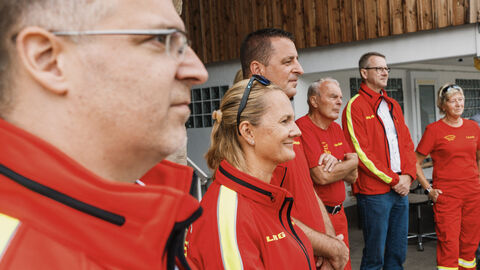 Mehrere Personen in rot-gelber Kleidung stehen vor einem Gebäude.
