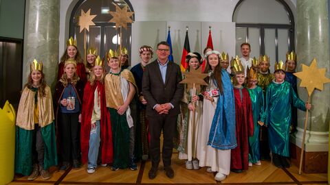 Ministerpräsident Boris Rhein steht gemeinsam mit einer Gruppe Kindern in Sternsinger-Kostümen in einem Raum der Staatskanzlei.