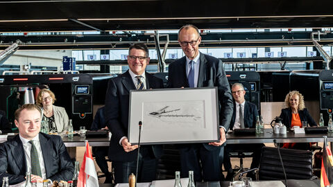 Zwei Männer stehen im Terminal im Frankfurter Flughafen nebeneinander und halten ein Bild hoch.
